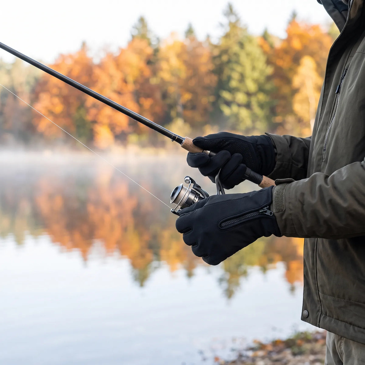 Angler wearing the Grip heated gloves holding a fishing rod by an autumn lake